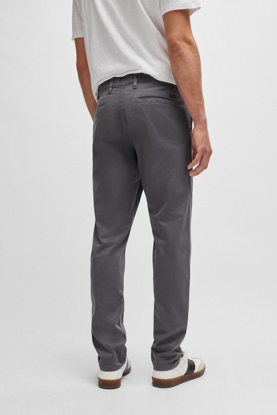 Een man draagt een antracietkleurige chino, van achteren gezien. De broek heeft een rechte pasvorm en sluit aan op de kuiten.