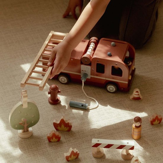 Kind speelt met houten brandweerwagen, ladder, poppetjes, boom, hydrant en vuurelementen.