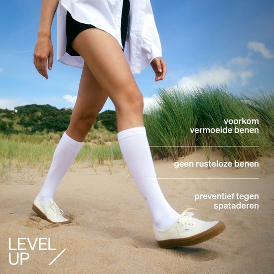 Vrouw loopt op strand met witte STOX Energy Socks, die spataderen voorkomen.