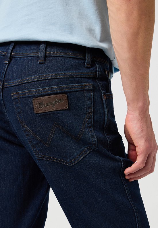 Close-up van de achterkant van een donkerblauwe jeans met Wrangler logo.