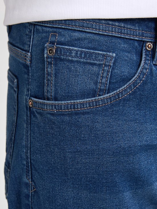 Detailopname van de spijkerbroek met naden, klinknagels en een muntzakje.