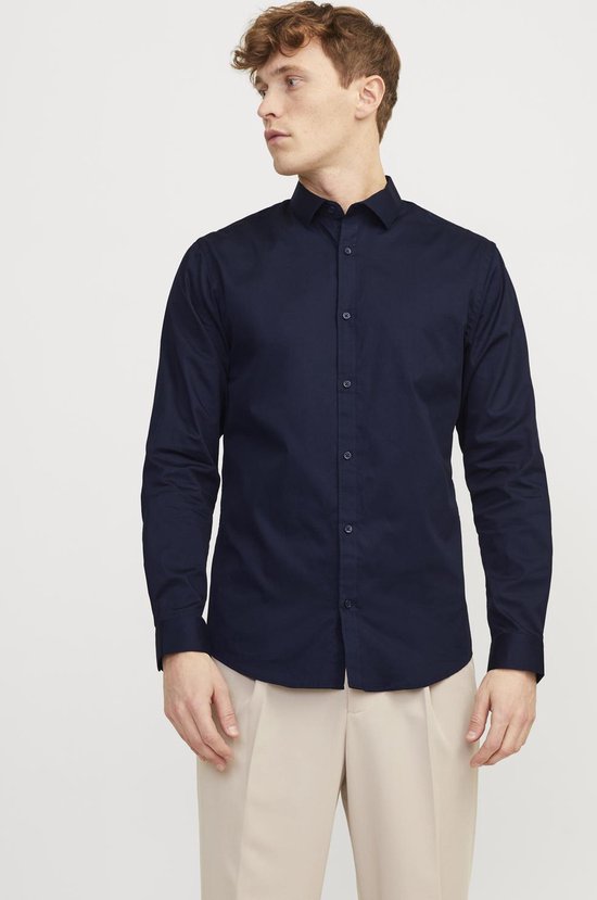 Man met marineblauw overhemd en beige broek, staand, voorkant.