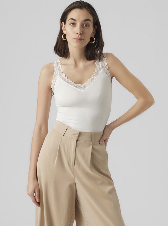 Model met de hand in de zak van een beige wijde broek, draagt wit kanten hemdje.