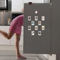 Een vrouw in een gestreepte jurk kijkt naar tien magnetische fotolijstjes op een koelkast.