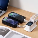 Wit 8-poorts USB oplaadstation laadt twee iPhones op met witte kabels, naast een laptop en tijdschrift.