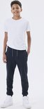 Jongen in wit t-shirt en donkerblauwe joggingbroek met grijze veters.