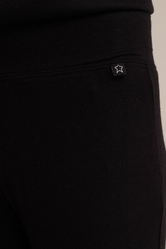 Een meisje draagt een zwarte trui met decoratieve witte randen aan de mouwen, een blauwe spijkerrok met plooien en gerafelde zoom, en zwarte laarzen.