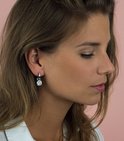 Model draagt een zilveren oorbel met een vierkante, witte hanger.