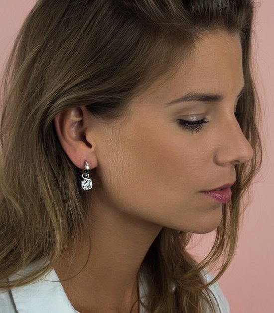 Model draagt een zilveren oorbel met een vierkante, witte hanger.