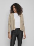 Lichtbeige gebreid vest met lange mouwen, gedragen over een wit shirt en zwarte leren broek.