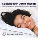 Vrouw met krullend haar glimlacht en rust op een Soulsnooze kussen.