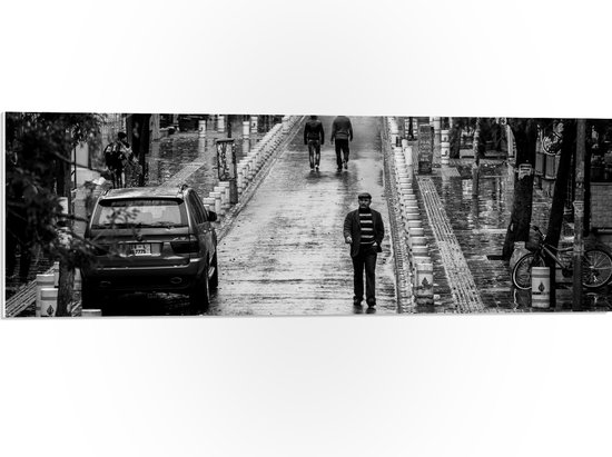 WallClassics - PVC Schuimplaat - Man wandeldn door Dorpje (zwart/wit) - 90x30 cm Foto op PVC Schuimplaat (Met Ophangsysteem)