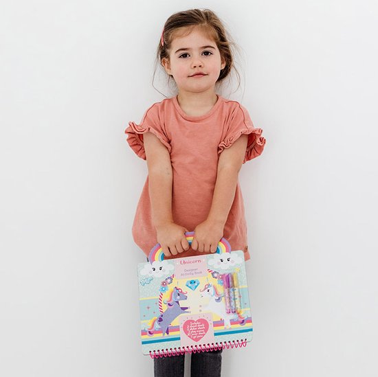 Une jeune fille dans une robe rose à volants tient un livre d'activités créatives Licorne avec une poignée arc-en-ciel.