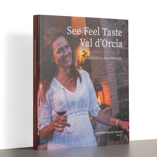 Een boek met de titel 'See Feel Taste Val d'Orcia, My Hidden Gems in Tuscany Part 1' en een foto van een lachende vrouw met een glas rode wijn.