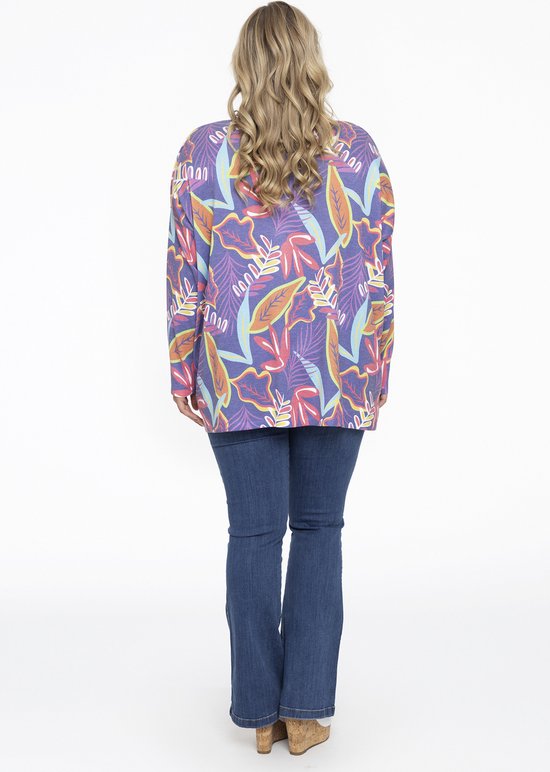 Vrouw met blond haar, achterkant, draagt een paars shirt met bladerprint en een spijkerbroek.