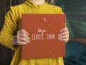 Een kind met een geel jurkje houdt een roestbruin boek vast met de tekst 'Mijn EERSTE JAAR', maan en sterren.