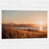 WallClassics - Muursticker - Zon Verdwijnend achter Bergen bij Strand - 75x50 cm Foto op Muursticker