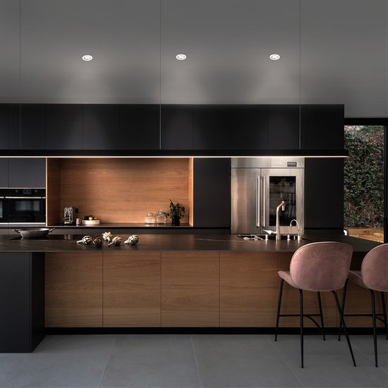 Moderne zwarte en houten keuken met inbouwspots en roze barkrukken.