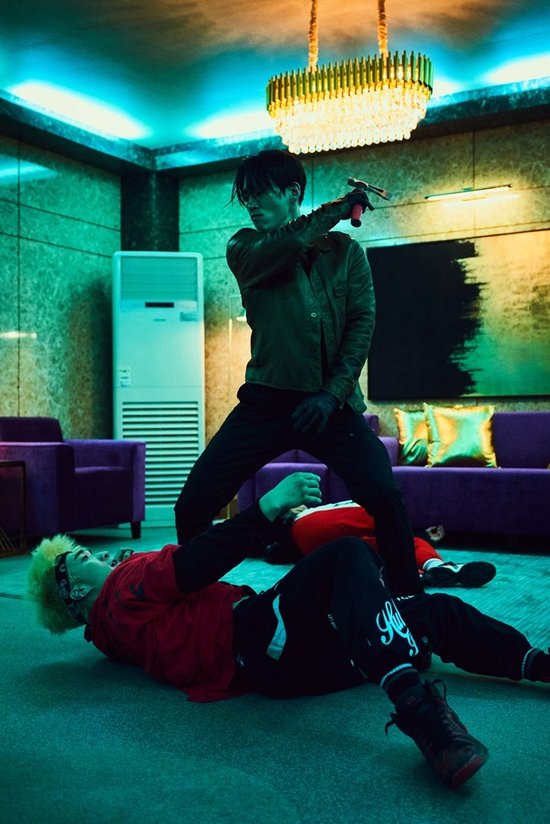 Man in groen jack met blonde man op de grond. Man met pistool in een kamer met paarse banken.