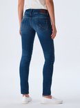 Achterkant van een model met een witte top, draagt een donkerblauwe, nauwsluitende jeans en witte instappers.