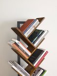 Detail van een boekenkast met houten takken waarop verschillende boeken staan. De ruggen van de boeken hebben titels zoals 'BAY LIVING'.