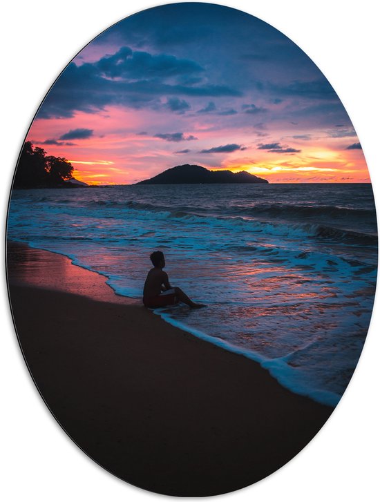 WallClassics - Dibond Ovaal - Persoon zittend op Strand met Zonsondergang - 72x96 cm Foto op Ovaal (Met Ophangsysteem)