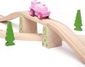 Roze en paarse speelgoedtrein op een houten brug met groene bomen.