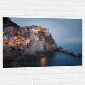 WallClassics - Muursticker - Verlicht Gekleurd dorpje aan Water - 105x70 cm Foto op Muursticker
