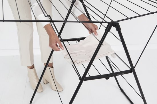 Vrouw met beige broek en witte schoenen legt een wit kledingstuk op het zwarte Brabantia HangOn droogrek.