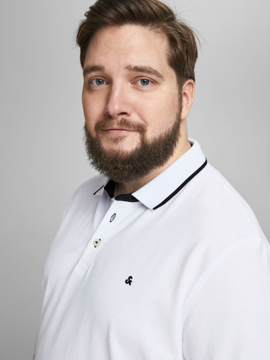 Man met blauwe ogen, baard, draagt een wit poloshirt met donkerblauwe kraagrand.