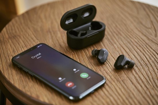 Zwarte oortelefoons en oplaadcase naast een smartphone met een oproepscherm.