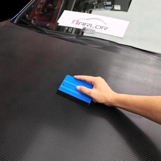 Hand die een blauwe rakel gebruikt op een matzwarte auto.
