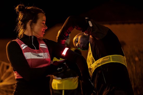 Vrouw met reflecterende Rogelli sportarmband met rode LED op arm. Man met reflecterend geel hesje.