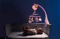 Baby in een co-sleeper kijkt omhoog naar een roze muziekmobiel met een lachende maan.