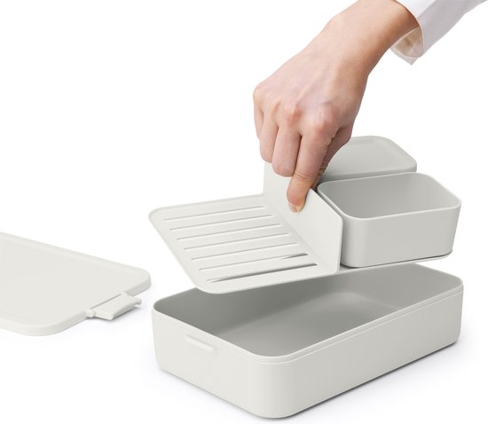 Main insérant une grille de séparation dans une boîte à pain grise. Boîte et compartiments ouverts.