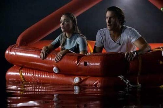Een man en een vrouw in een oranje reddingsvlot op het water, met bezorgde gezichten.