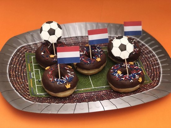 Vijf chocolade donuts met Nederlandse vlaggetjes en voetbalprikkers op een stadion-bord.