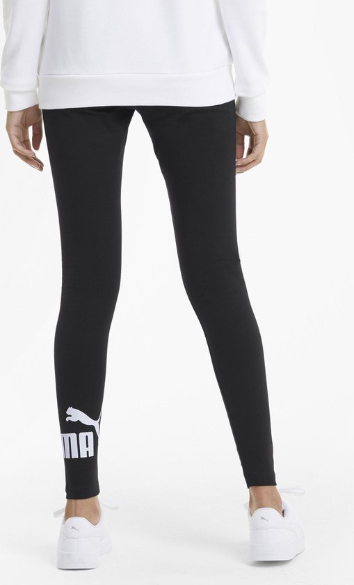 Gezichtspunt van achteren van een vrouw in zwarte legging met lichtpaars Puma-logo op de zijkant, gedragen met witte sneakers.