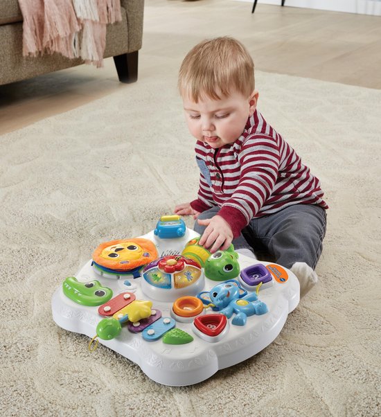 Een jongetje speelt met een witte speeltafel met dieren en gekleurde knoppen.