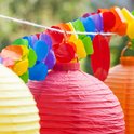 Een rode en een oranje papieren lampion met een regenboog slinger op de achtergrond.