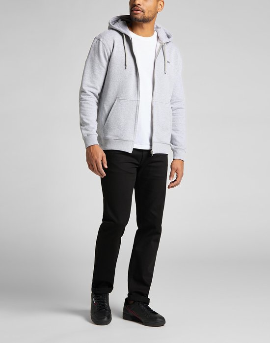 Man in zwarte jeans en grijze hoodie, staand.