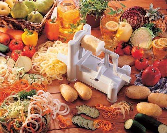 Witte spiraalsnijder met diverse groenten zoals courgette, wortel, ui, aardappelen, tomaten en kool op een houten tafel.