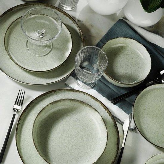 Lichtgroen aardewerken serviesgoed met donkere randen, bestek en glazen op marmeren tafel.