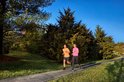 Man en vrouw rennen op een pad in een park, beiden dragen Garmin sporthorloges. De vrouw draagt een roze shirt, de man een oranje shirt.