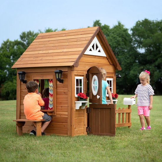 Kinderen spelen in en rondom het houten speelhuis Aspen, met brievenbus en buitenbankje.