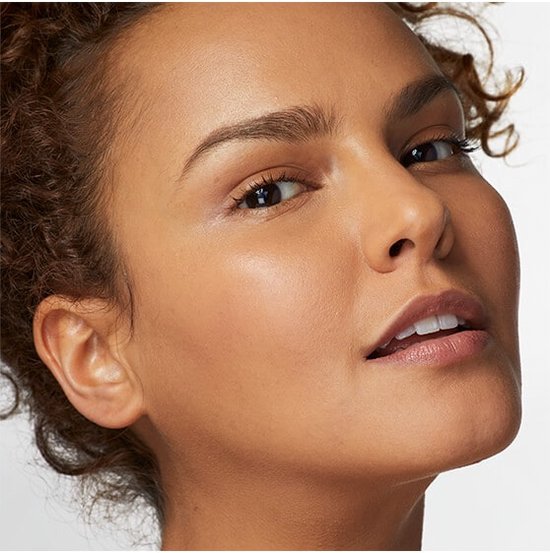 Close-up van een vrouw met medium bruine huid, die een foundation draagt met een natuurlijke, dekkende finish.