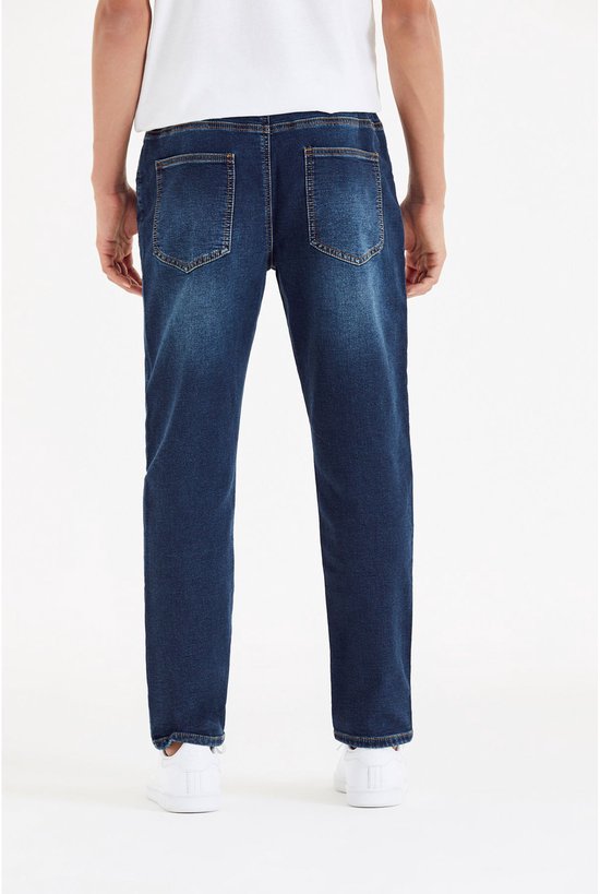Man draagt donkerblauwe jeans met elastische tailleband, trekkoord en kontzakken.
