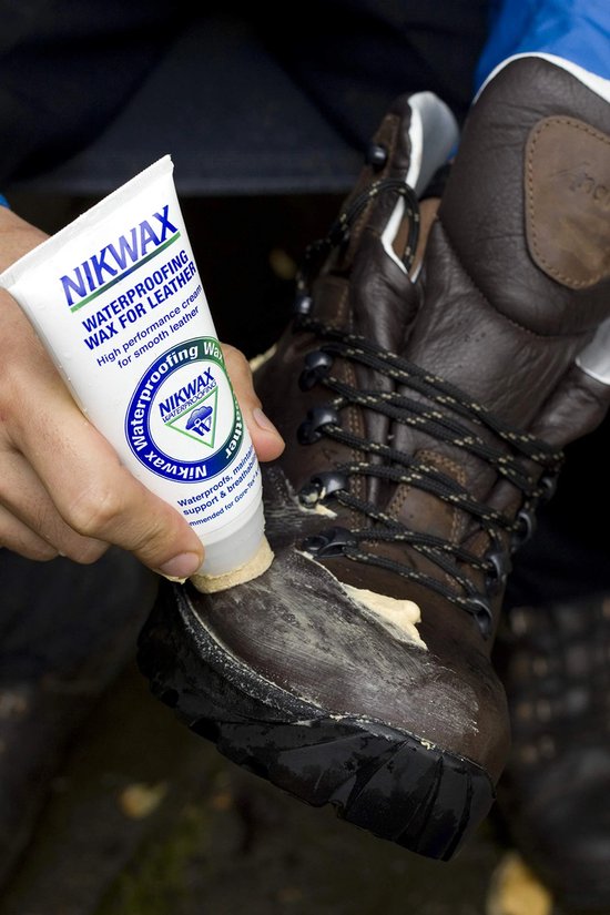 Hand brengt Nikwax waterdichtingswax aan op bruine leren wandelschoen.
