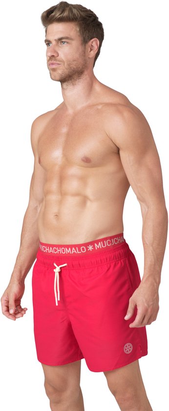 Man in rode zwembroek met witte tailleband 'MUCHACHOMALO' en een logo.