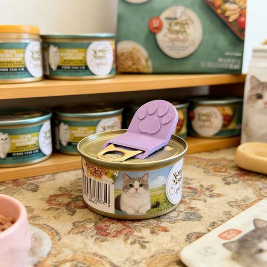 Paarse pootvormige blikopener op een blik kattenvoer, omringd door kattenvoerproducten.